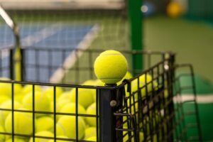 Yellow Tennis Ball close up on the edge of a black cart with tennis balls on the tennis court, Pinterest